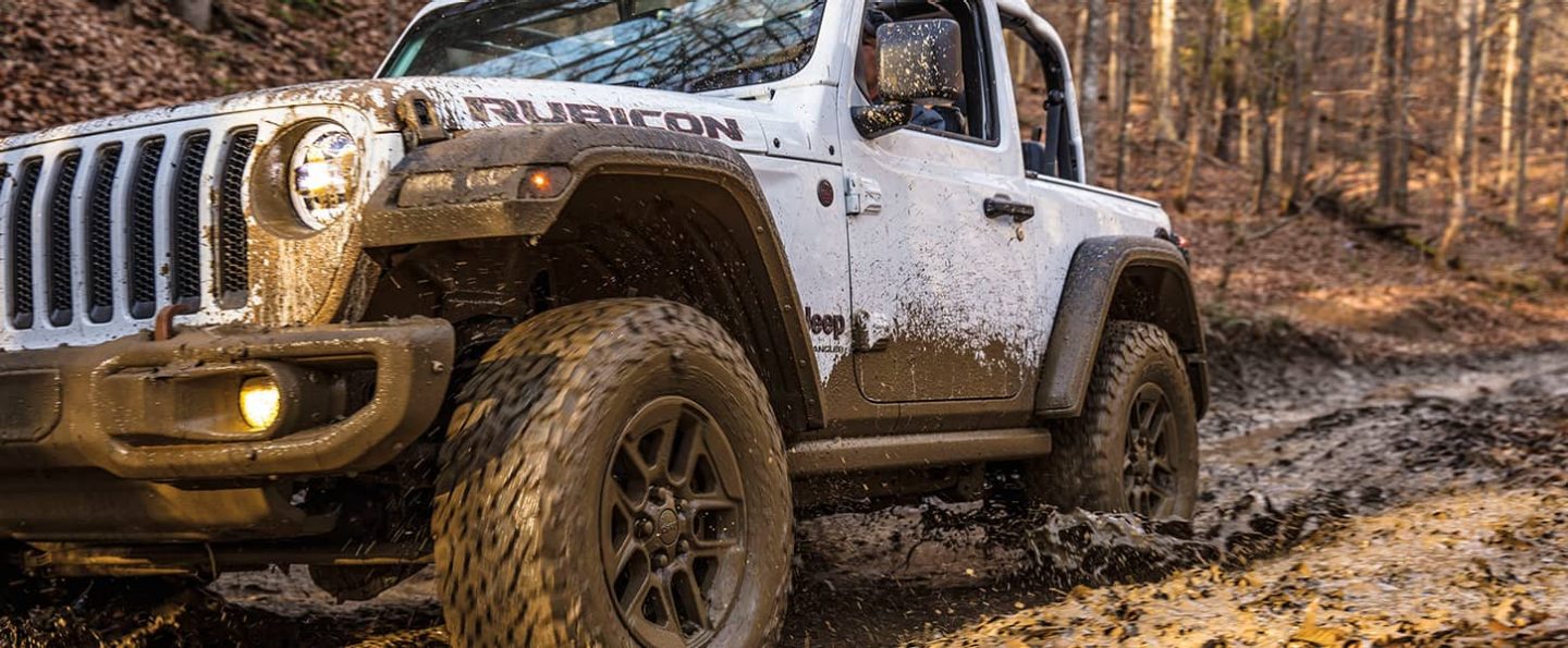 A mud-spattered 2021 Jeep Wrangler Rubicon being driven on a trail.