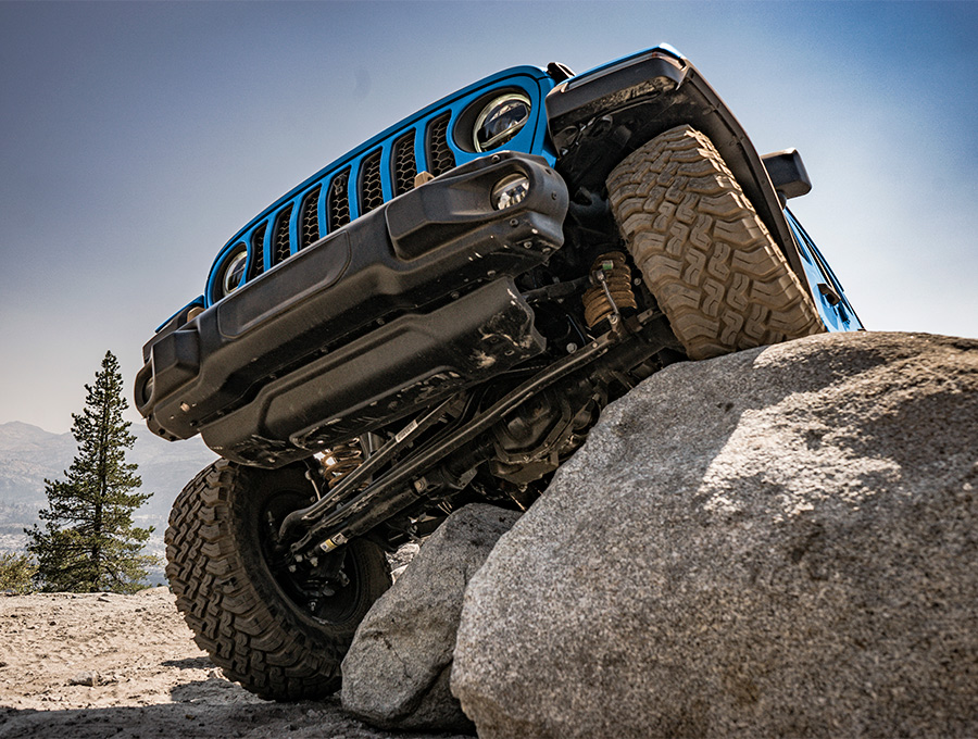 A view from below, of the front axle on the 2021 Jeep Wrangler Rubicon 392, as one wheel climbs a large rock and the other wheel stays on the ground.