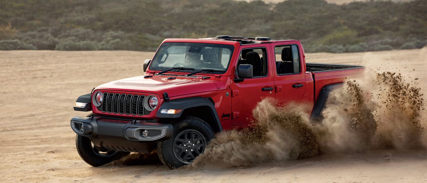 An olive green 2025 Jeep Gladiator Rubicon X crawling over a series of boulders in a forest off-road.