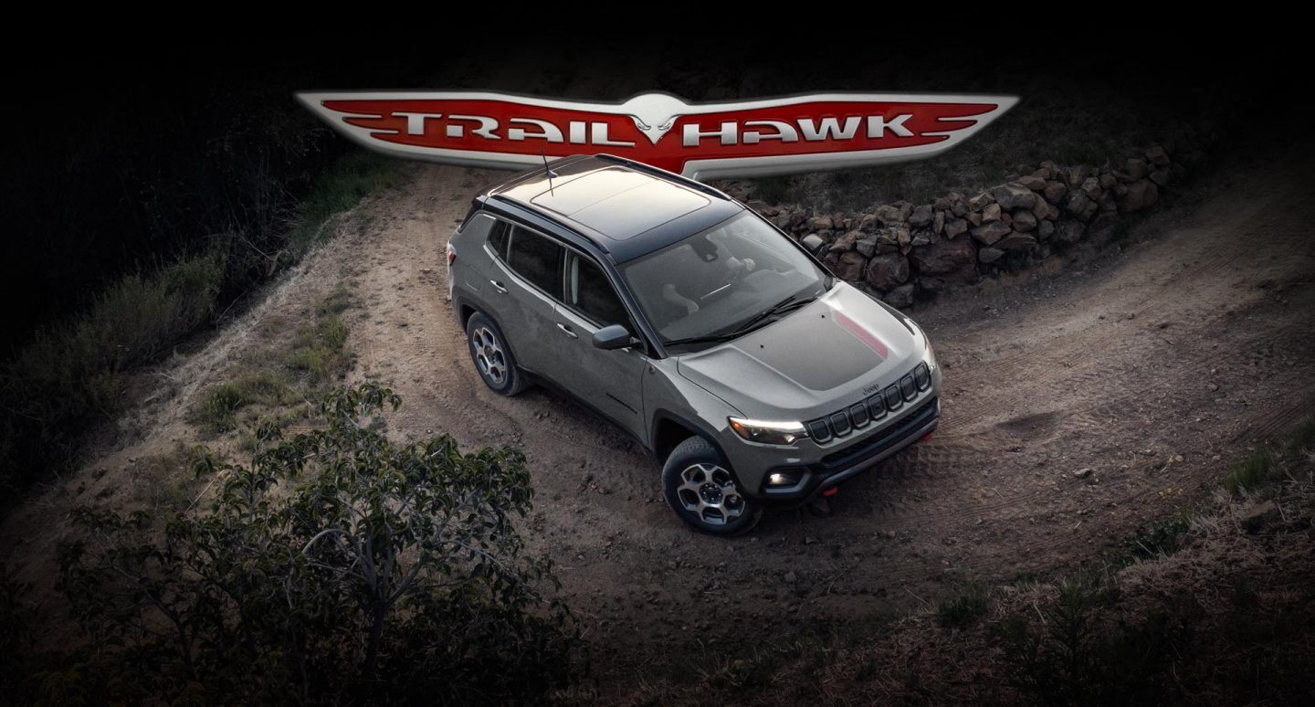 Trailhawk logo. The 2022 Jeep Compass Trailhawk rounding a curve on a dirt road.